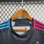 Black athletic jersey on a wooden hanger with blue shoulder stripes on the left and pink stripes on the right, size XL, against a metal grid backdrop, with a small star emblem visible.