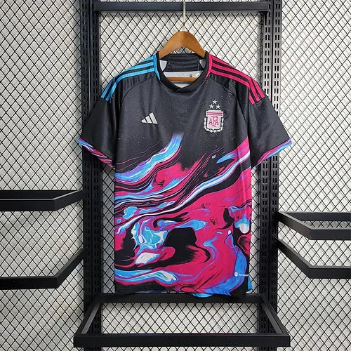 Black Adidas Argentina soccer jersey with a bold pink, blue, and white swirl design, hanging on a wooden hanger against a metal grid display.