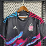 Black Adidas soccer jersey on a hanger with the Argentina Football Association crest, blue shoulder stripes, pink accents, and a colorful abstract pattern on a metal rack.