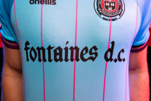 2124CFC8-BD19-4CEA-A808-C78AAAAB90EE | UAE SPORT STORE Light blue rugby jersey with pink vertical stripes and the text 'fontaines d.c.' across the chest, plus a crest on the upper right side of the shirt.