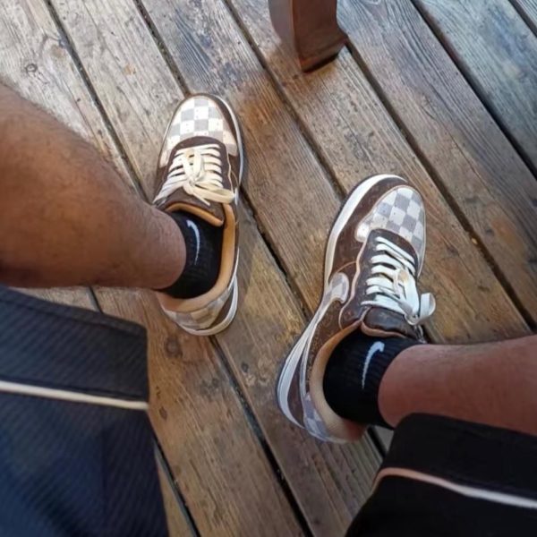 Two people wearing brown-and-beige checkered sneakers stand on a weathered wooden deck, viewed from above.