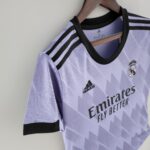Lavender Real Madrid football jersey hanging on a wooden hanger, showing Adidas logo and club crest on the chest area.”