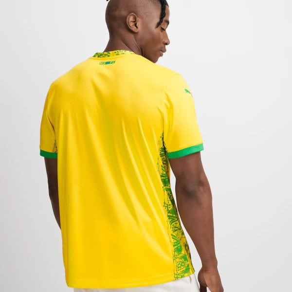 Back view of a man wearing a bright yellow sports jersey, with green sleeve cuffs and a green tropical side panel, facing away.