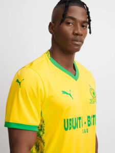 Portrait of a man wearing a bright yellow soccer jersey with a green collar, facing slightly to the right.