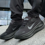 Close-up of black Nike Air Zoom sneakers with gray swoosh on a person standing on a concrete ledge.