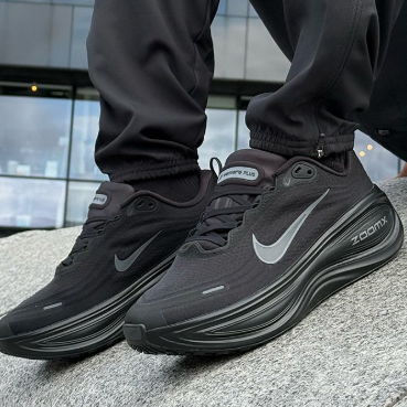 Close-up of black Nike Air Zoom sneakers with gray swoosh on a person standing on a concrete ledge.