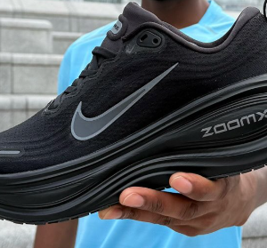 Black Nike ZoomX running shoe held by a person in a blue shirt, showing the Nike swoosh against a stair background.