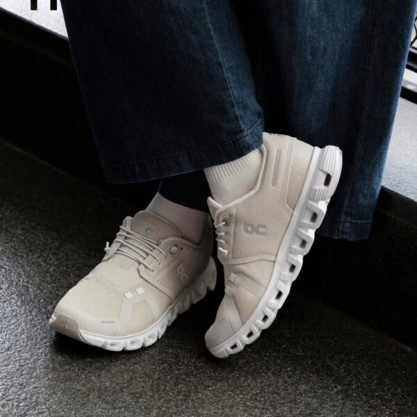 Cream-colored athletic sneakers with a chunky segmented sole, worn with white socks and dark jeans.