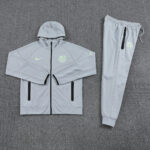 Light gray Nike Barcelona training jacket with a hood and neon crest, paired with matching jogger pants laid flat on a gray carpet.