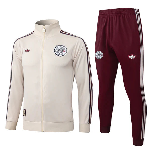 Beige Adidas zip-up track jacket with navy stripes and crest, paired with burgundy track pants with white side stripes and logos.