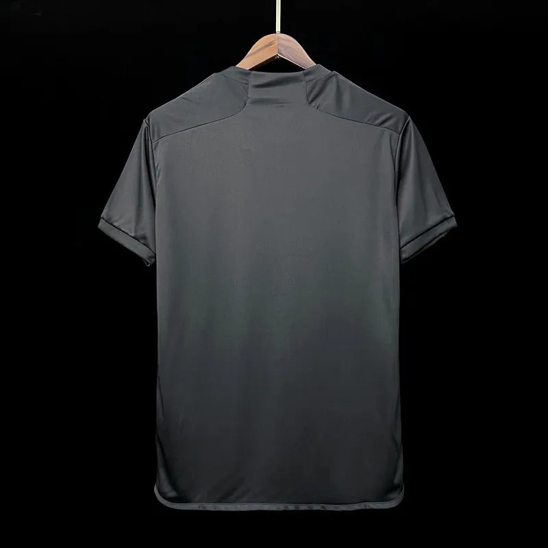 22ba0666d6ec9f5b_3ff645a7-a8bc-400b-991b-48126aa03dac | UAE SPORT STORE Dark gray short-sleeve polo shirt shown from the back, hanging on a wooden hanger against a black background.