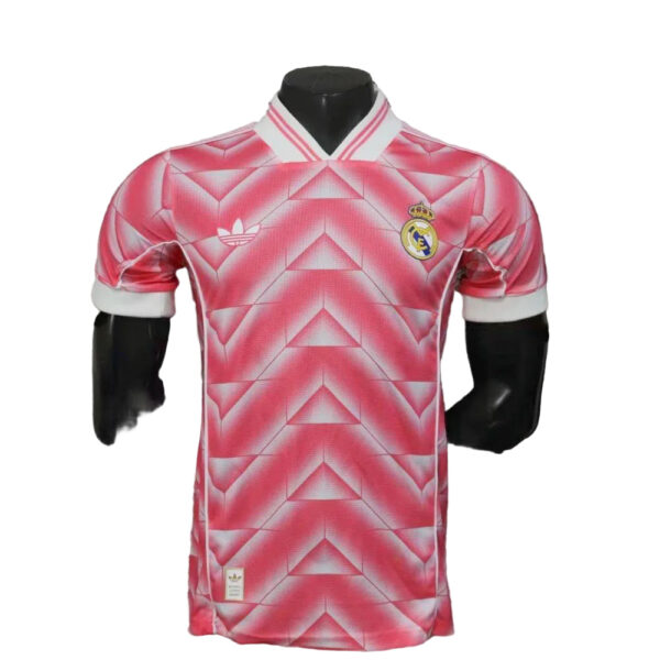 Pink Real Madrid soccer jersey with geometric pattern on a mannequin, white collar and Real Madrid crest on the chest.