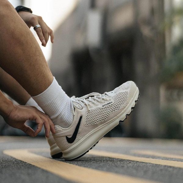 Close-up of a white running shoe with a black Nike swoosh being tied on a street with yellow road markings nearby.