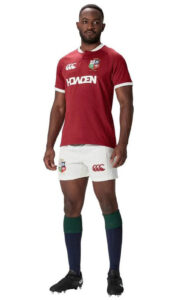 Rugby player in red jersey and white shorts, standing with hands at sides, wearing dark socks and boots.
