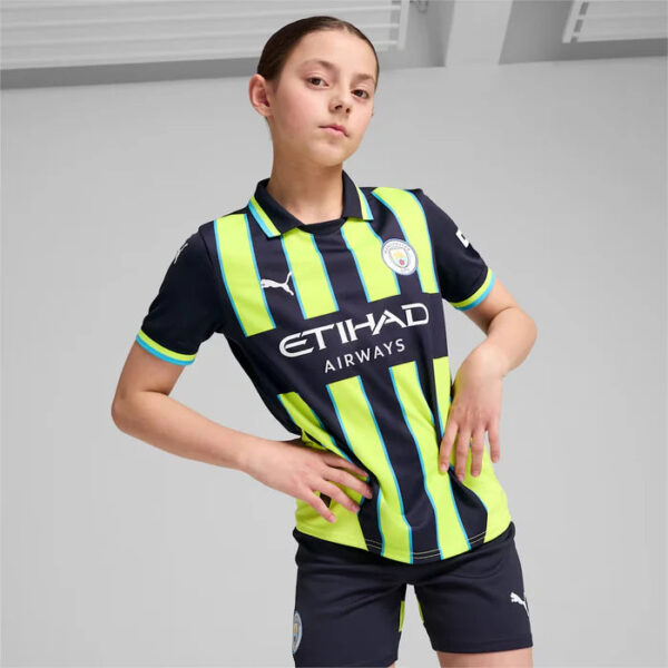 Young girl posing in Manchester City kids football kit with neon-yellow and navy stripes, sponsor logo Etihad Airways on the shirt.