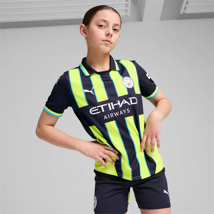 25-Away-Replica-Big-Kids_-Soccer-Jersey_5_700x700_d5b9eb19-4487-4311-886c-7f91f1dc9ed1 | UAE SPORT STORE Young girl posing in Manchester City kids football kit with neon-yellow and navy stripes, sponsor logo Etihad Airways on the shirt.