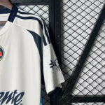 White athletic jersey hanging on a chain-link fence, with dark shoulder stripes and a circular logo on the chest.