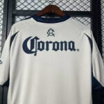 White baseball jersey on a hanger displaying a large navy Corona logo on the back, with a small crest above it.