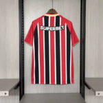 Red, black, white striped jersey with SUPERBET on the back, hanging on a wooden hanger in a closet.