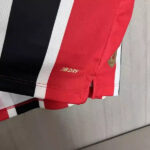 Close-up of red athletic shorts with NB DRY branding, alongside black and white color blocks, hanging on a light wood surface.