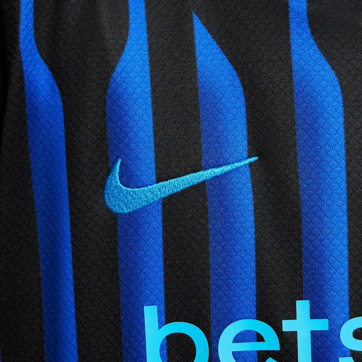 Close-up of a turquoise Nike swoosh embroidered on a black-and-blue striped sports jersey.