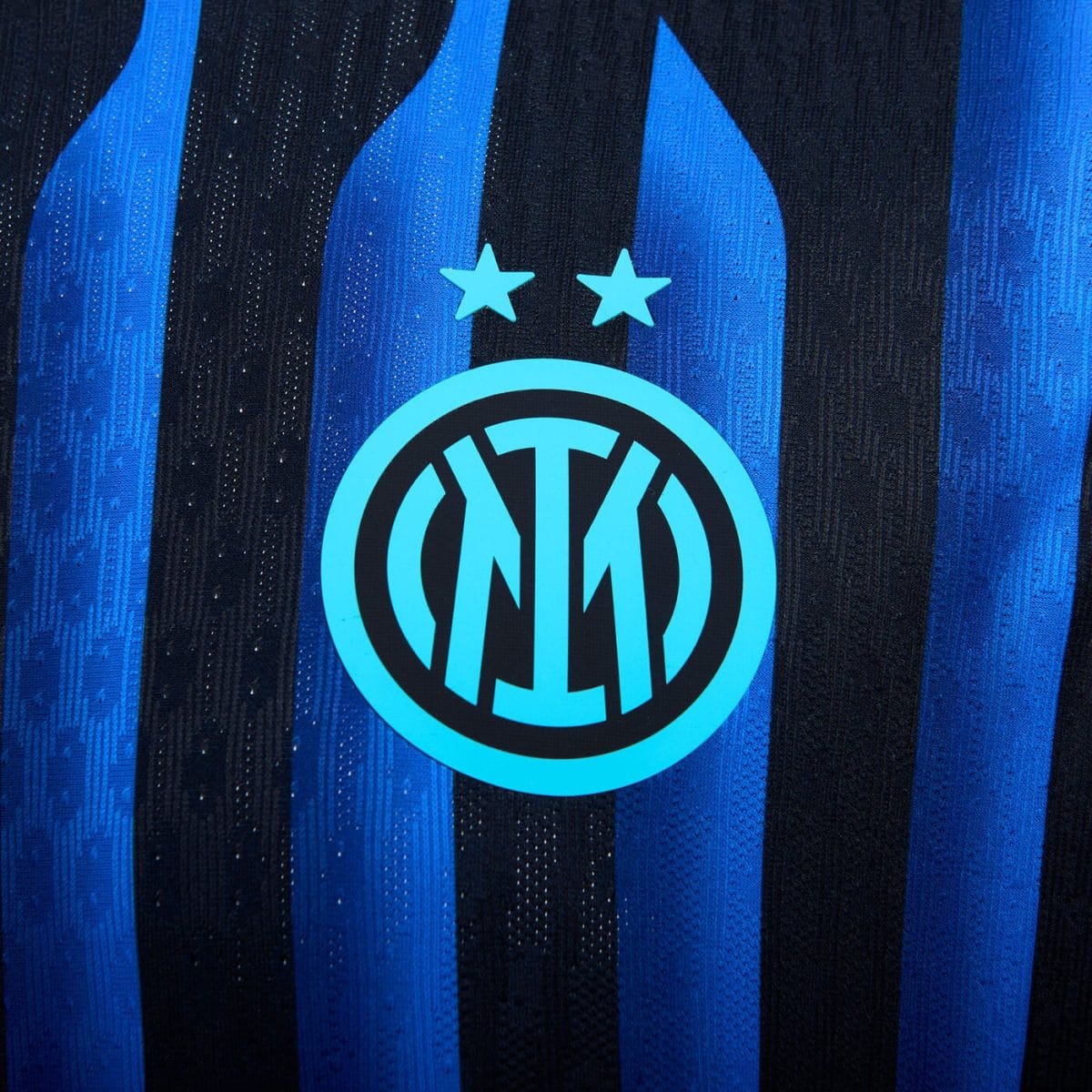 Inter Milan club crest on a blue-and-black striped jersey with two stars above it, shown in close-up.
