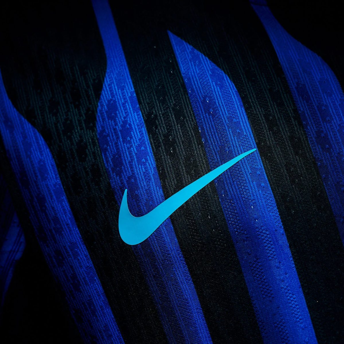 Close-up of a bright blue Nike swoosh on a blue-and-black striped fabric, likely part of a sports shoe or apparel