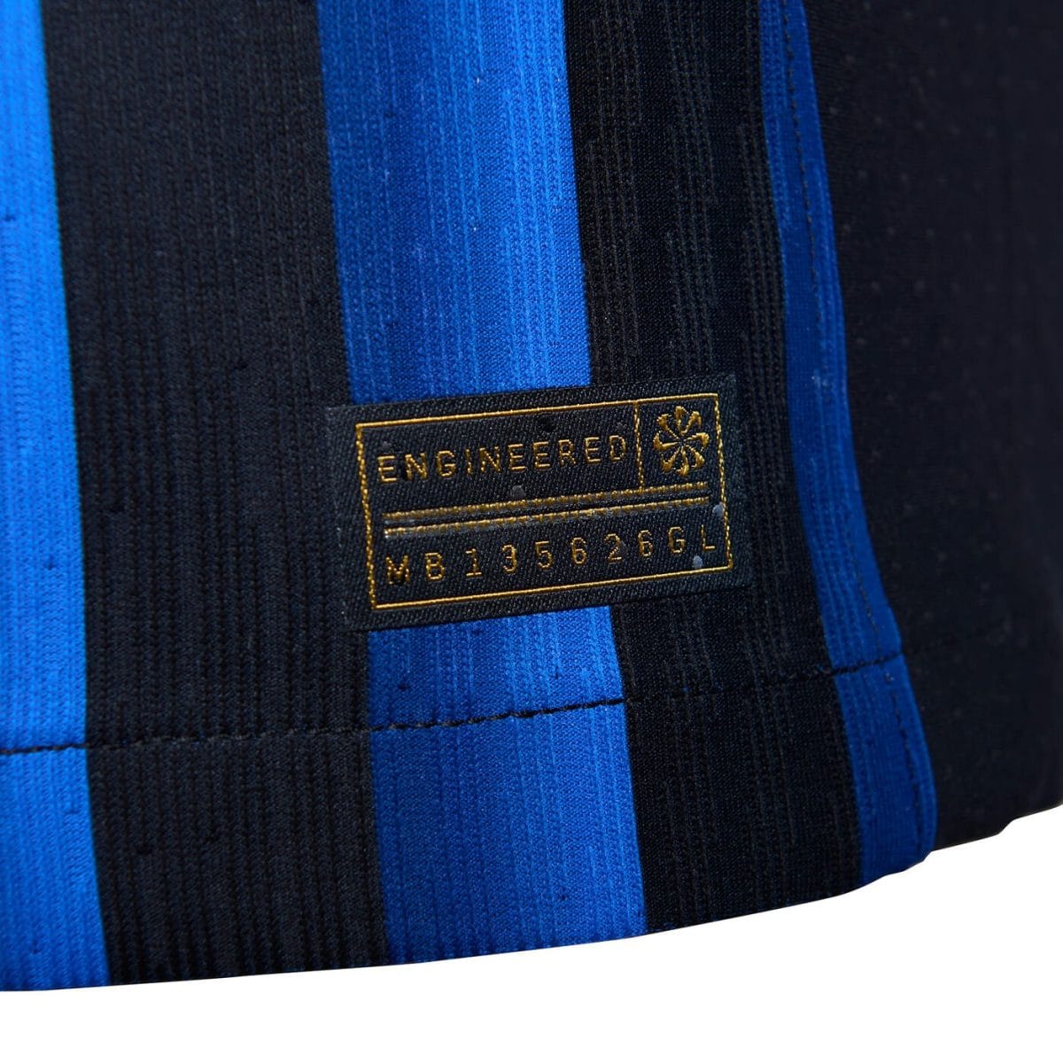 Close-up of blue and black striped fabric with a gold-embroidered label reading 'ENGINEERED' and a small emblem, on a garment edge.