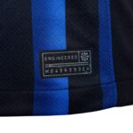 Close-up of a fabric tag on a black-and-blue striped material, reading 'ENGINEERED' with a small code beneath.