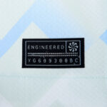 Black sewn label reading 'ENGINEERED' with a small emblem on the right and a row of numbers underneath, sewn onto light fabric