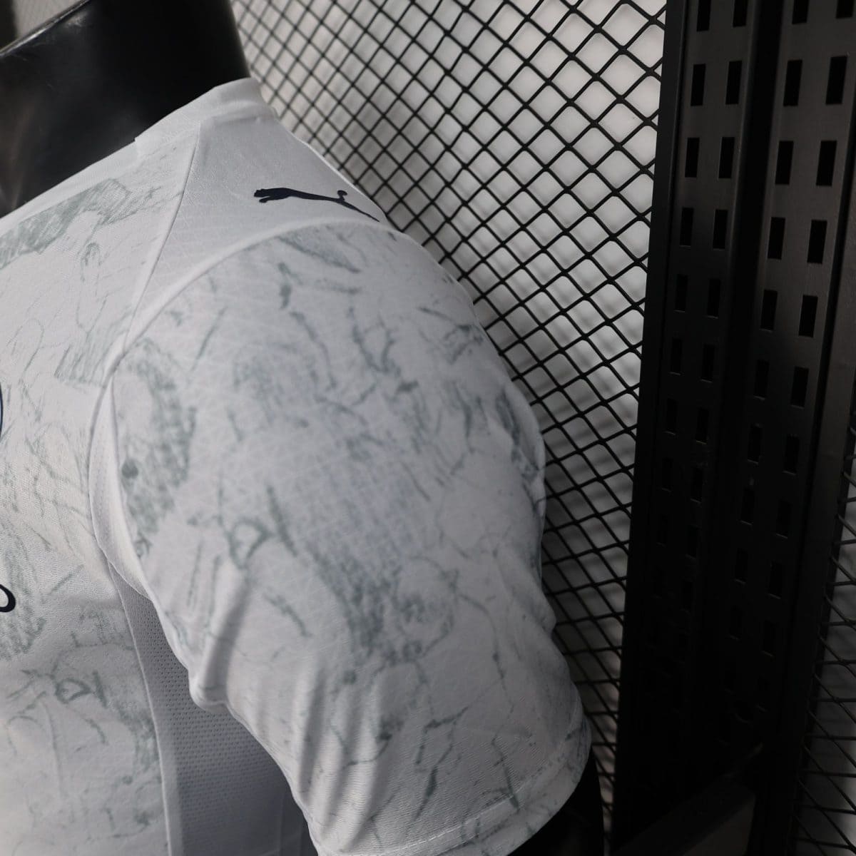 Close-up of a light camo-patterned shirt on a black mannequin against a diamond metal mesh backdrop.