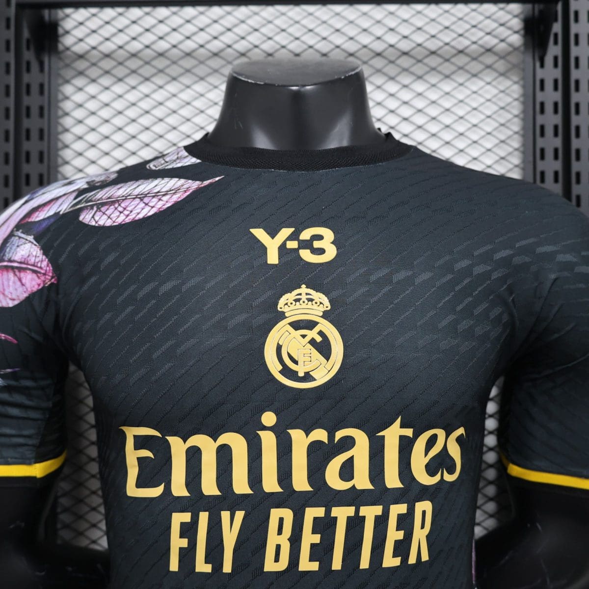 Close-up of a Real Madrid jersey chest showing the gold Real Madrid crest and Emirates Fly Better sponsor on a dark striped fabric.