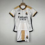 White Real Madrid jersey on a wooden hanger with gold stripes, featuring Adidas logo, club crest, and 'Emirates Fly Better' sponsor text.