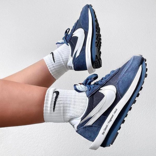 Blue and white athletic sneakers with a white midsole and black outsole, shown with white socks against a plain wall.