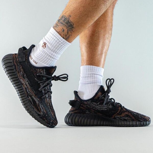 Person wearing black camo-pattern sneakers with white crew socks, standing on tiptoe for a product shot