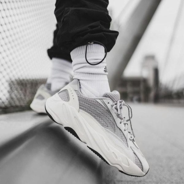 Close-up of white athletic sneakers and white socks as a person balances on a curb beside a bridge railing (black-and-white photo).