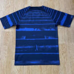 Navy blue short-sleeve athletic jersey laid flat on a wooden floor with horizontal light-blue stripes fading toward the bottom.