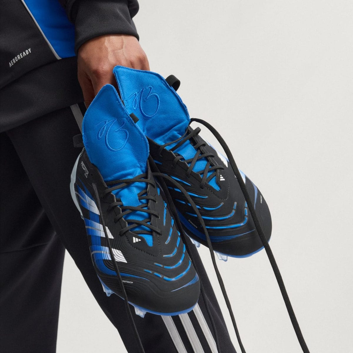 Close-up of blue and black athletic sneakers being held by a hand, showing laces and side pattern.