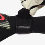 270046_Gallery_3_1348445 | UAE SPORT STORE Close-up of a black sports strap with Velcro being fastened, showing a plastic buckle and a red logo on the left.