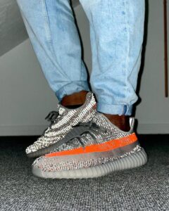 Person wearing light blue jeans and sparkly gray sneakers with an orange stripe, standing on a carpeted floor.