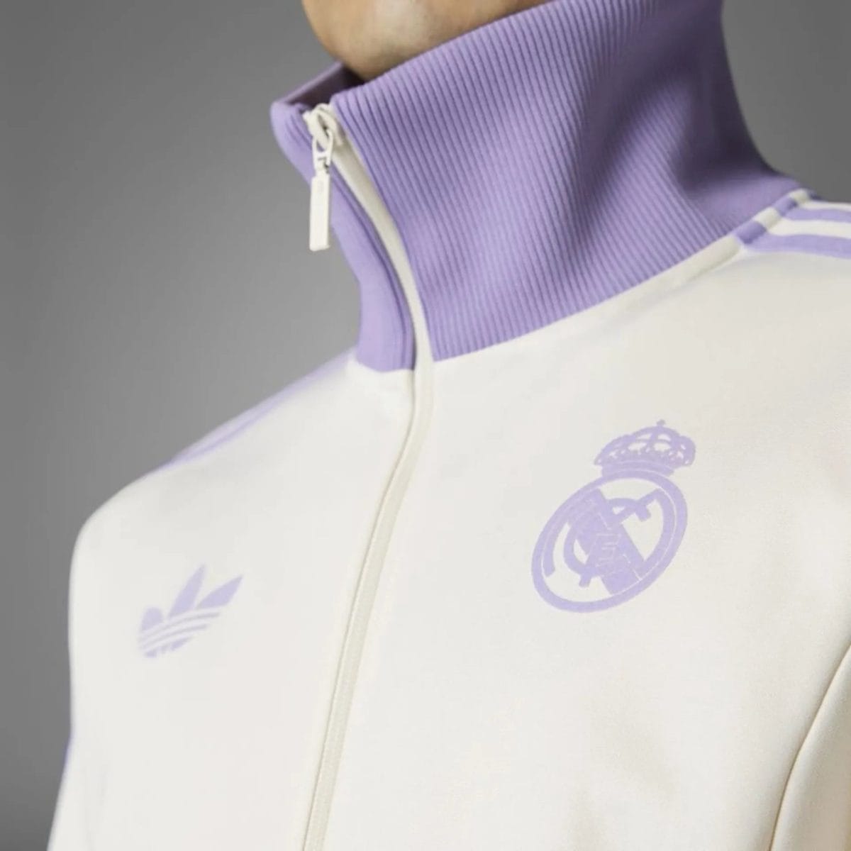 Close-up of a lavender zip-up collar on a white jacket, with a lavender Real Madrid crest on the chest.