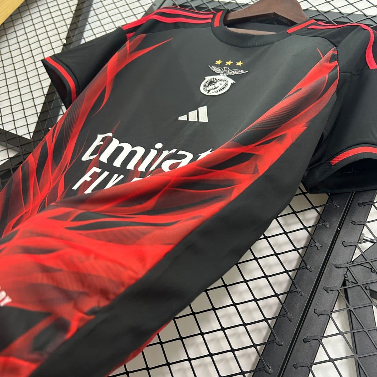 Black and red sports jersey hanging on a hanger, displaying a winged crest with four gold stars above it.