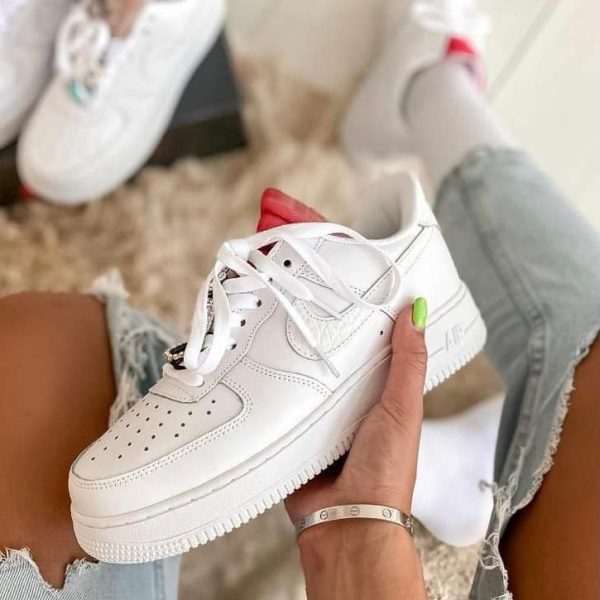 Person sitting with ripped jeans, holding a white Nike Air Force 1 sneaker; neon green nail visible on the thumb; other white sneakers in the background.