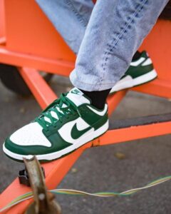 Close-up of a green and white Nike sneaker on a black sock, resting on an orange metal bench.