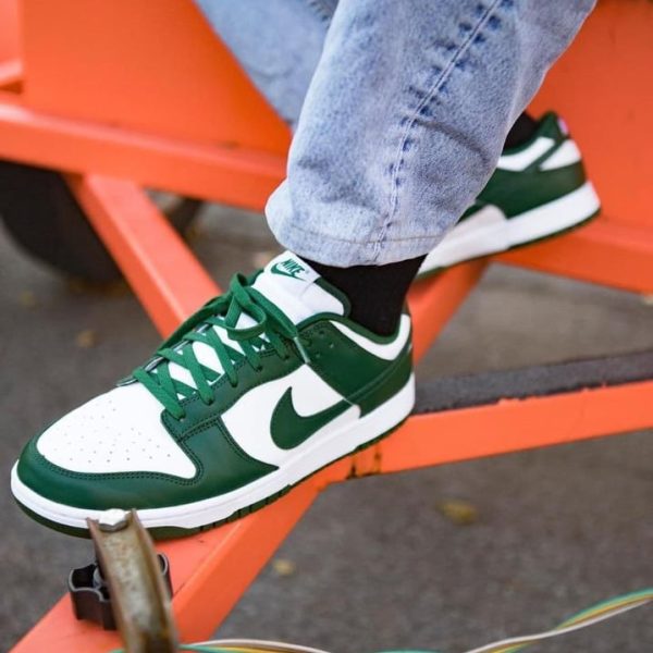 Close-up of a green and white Nike sneaker on a black sock, resting on an orange metal bench.