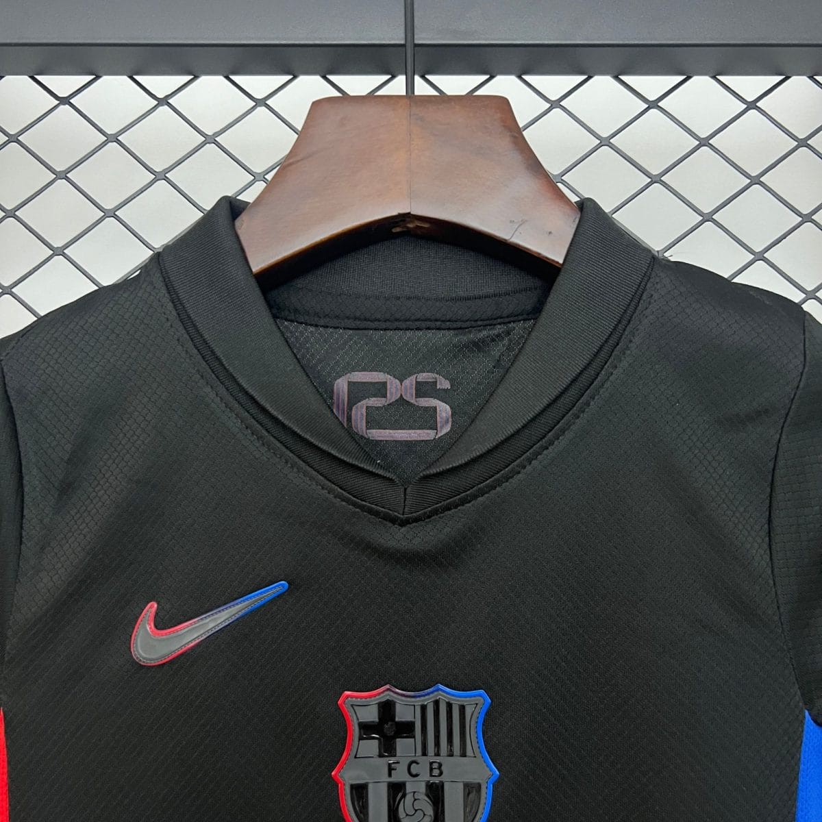 Black sports jacket on a wooden hanger with red and blue shield patches, against a chain-link fence.