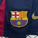 Close-up of the FC Barcelona crest embroidered on a dark blue jersey with a red stripe nearby, showing the shield and colors.