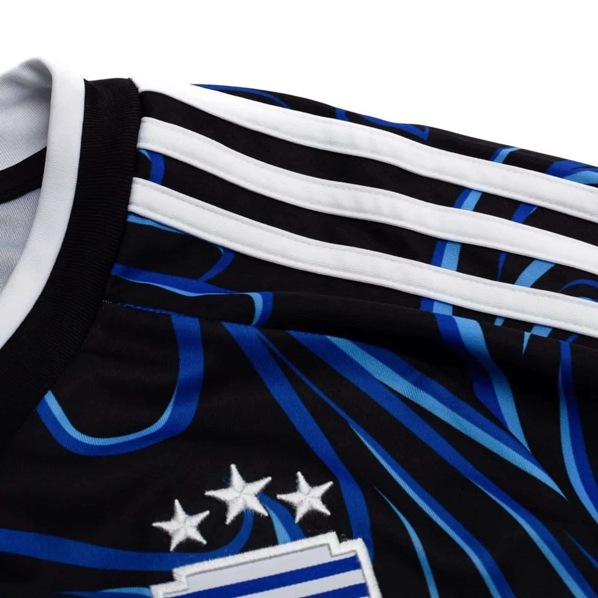 28746ed1311a | UAE SPORT STORE Close-up of a black jersey with white stripes, blue accents, and white star motifs visible behind the stripes.