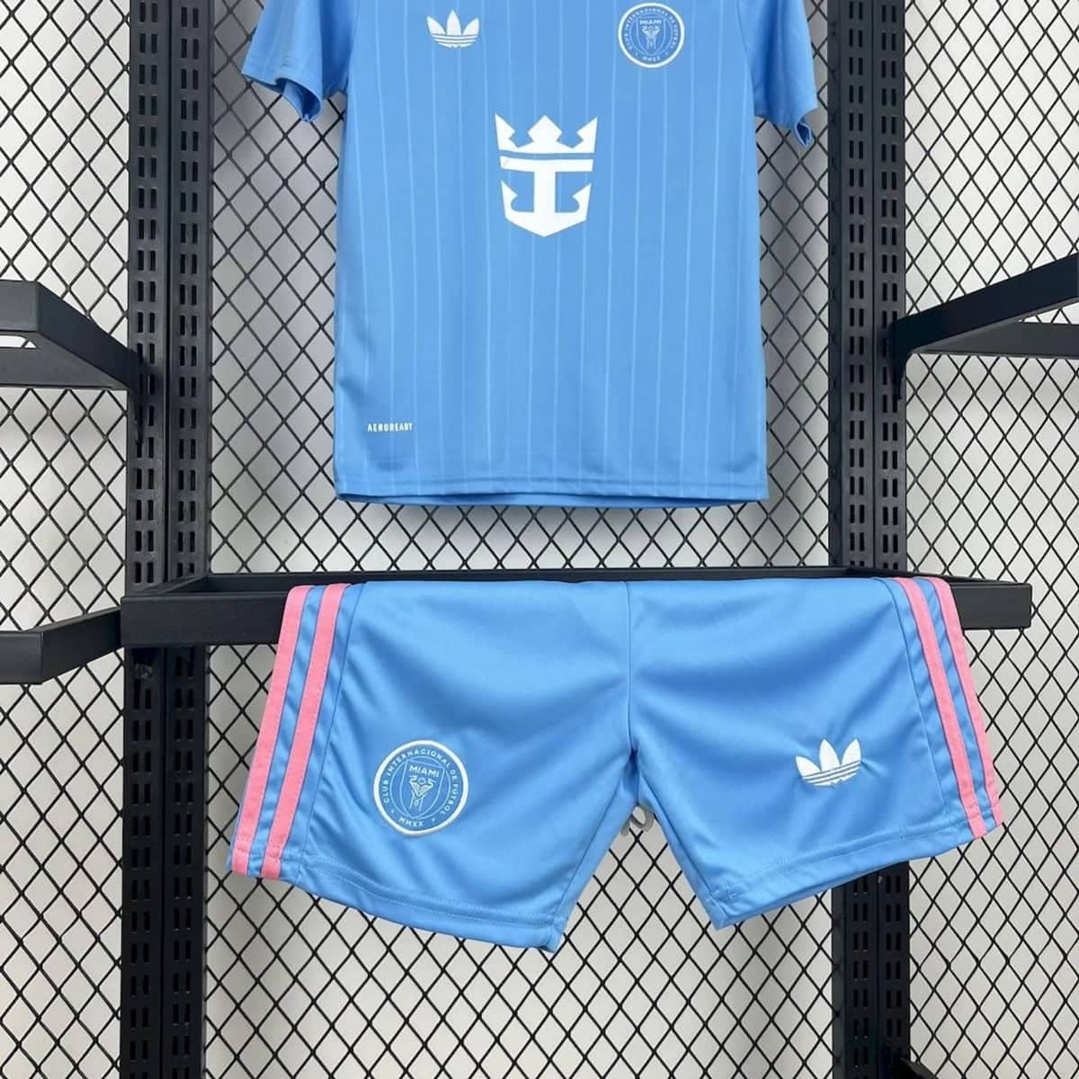 Blue athletic shorts with pink side stripes hanging on a display shelf, logos visible on the front.
