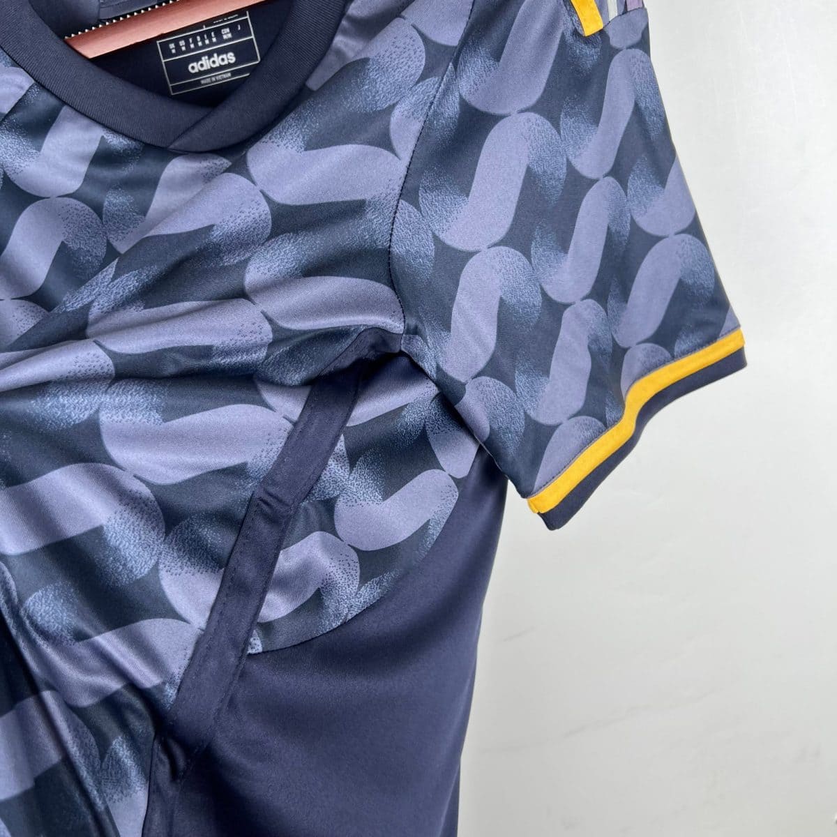 Close-up of a blue patterned Adidas jacket with yellow trim along the cuff and a label inside the neck area.